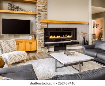 Furnished Living Room In Luxury Home With Roaring Fireplace, TV, Coffee Table, Rug, And Wrap-Around Couch