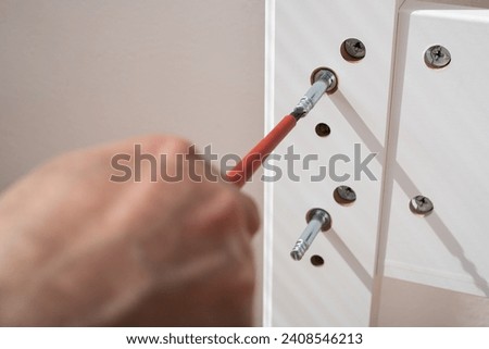 The furniture assembler assembles the bed frame, twists the fixers, hands with a close-up screwdriverputting together self assembly furniture.