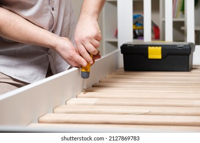 The furniture assembler assembles the bed, twists the screws on the wooden slats, hands with a close-up screwdriver