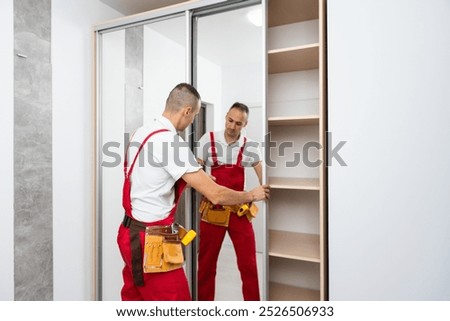 Furniture assembling. Professional worker installing wardrobe at living room of new house.