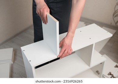Furniture assembly. The furniture assembler takes a white shelf, tightens the screw with a hex wrench.Collector of furniture.Moving concept, furniture assembler, self assembly