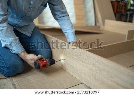 Furniture assembly process. Assembling new bed for the bedroom. Young man assembles a wooden bed using a screwdriver in a stylish home interior. Self-made home furniture.