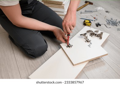 Furniture assembly. A worker is screwing a hinge with a screwdriver into a wooden closet door. Adjustment of fittings - Powered by Shutterstock