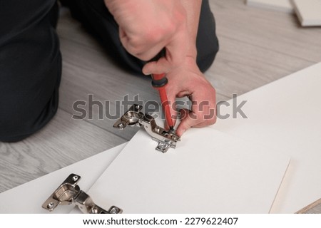 Furniture assembly. A worker is screwing a hinge into a wooden cabinet door with a screwdriver. Adjustment of fittings, door hinges. The concept of installing furniture, home renovation. [[stock_photo]] © 
