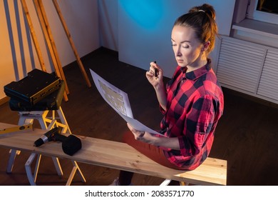 Furniture Making Designer Concept. Woman With Architectural Plan. Girl Furniture Maker In Casual Uniform. Carpenter Woman. Planks Beside Woman Carpenter. Girl Furniture Maker In Carpentry Workshop