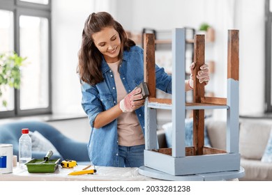 furniture renovation, diy and home improvement concept - happy smiling woman sanding old wooden table with sponge