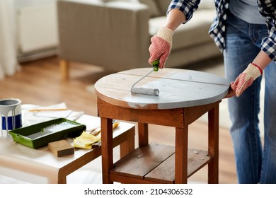 furniture renovation, diy and home improvement concept - close up of woman in gloves with paint roller painting old wooden table in grey color - Powered by Shutterstock