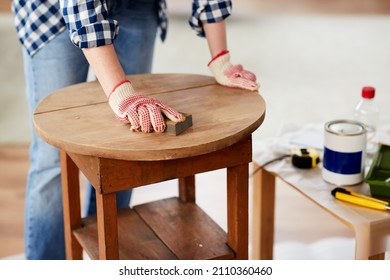 furniture renovation, diy and home improvement concept - close up of woman sanding old wooden table with sponge