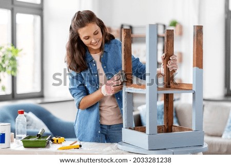 furniture renovation, diy and home improvement concept - happy smiling woman sanding old wooden table with sponge
