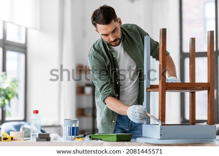 furniture renovation, diy and home improvement concept - man in gloves with paint brush painting old wooden table in grey color