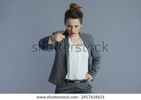 fury trendy 40 years old woman employee in grey suit threatening with finger isolated on gray.