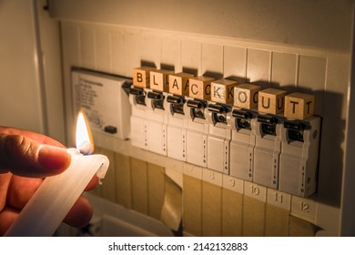 Fuse box with fuses in a distribution box during a power outage lit with white candle holding a man with the word blackout as text, Germany - Shutterstock ID 2142132883