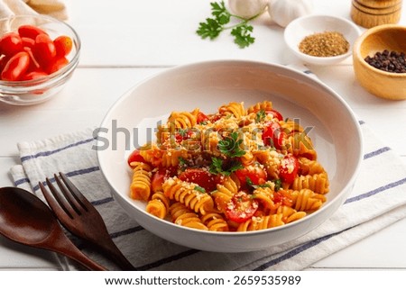 Fusilli macaroni with fresh cherry tomatoes and tomato sauce topped with parmesan cheese and chopped parsley leaves in a plate.