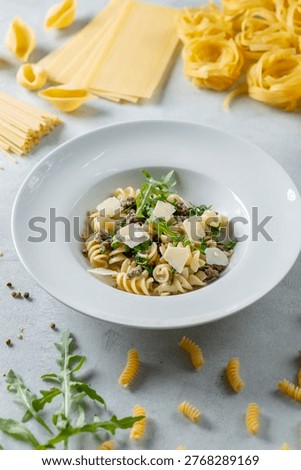 Fusilli pasta serving with ground meat, pecorino cheese, and arugula on a white plate
