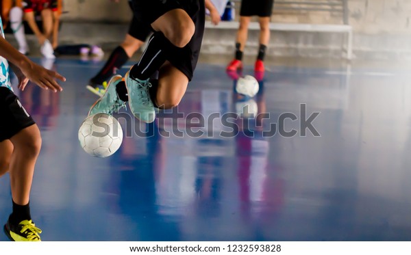 Futsal player  jump with trap and control the ball\
for shoot to goal. Soccer players fighting each other by kicking\
the ball. Indoor soccer sports hall. Football futsal player, ball,\
futsal floor.