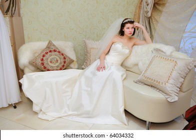 Future Bride In Wedding Dress Sitting On Sofa At Bridal Shop