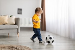 Future Champion. Adorable Little Toddler Boy Playing Football, Hitting Ball At Home, Having Fun In Living Room Interior, Copy Space