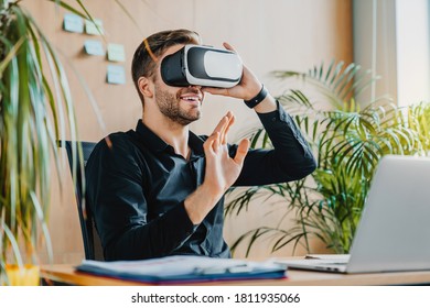 Future Concept. Handsome Young Man In VR Headset Gesturing And Smiling While Sitting In Office