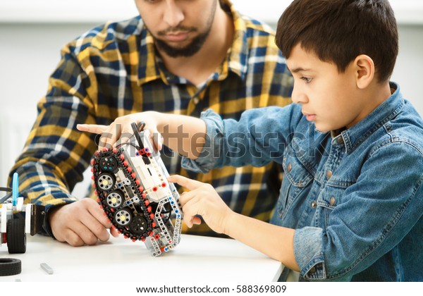 Future engineer. Young African American boy\
looking serious and concentrated while repairing his remote control\
robotic car with his father sitting near family hobbies activities\
children childhood 