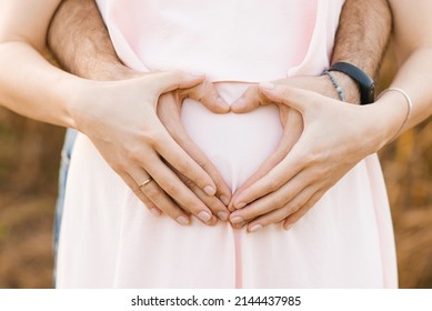 The future father hugs the belly of a pregnant woman, the expectant mother and makes hands with her in the form of a heart. Care and love for the child