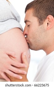 Future father kissing the belly of his pregnant wife both in the bedroom
