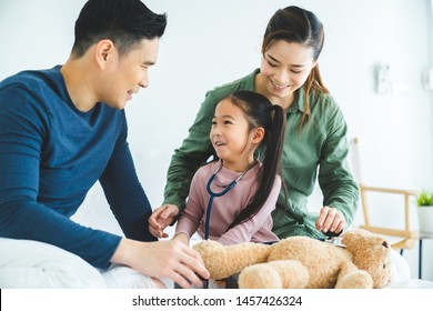 Future Little Daughter Playing Doctor Consulting With Parents Sitting On Bed And Happy Family Having Fun Together