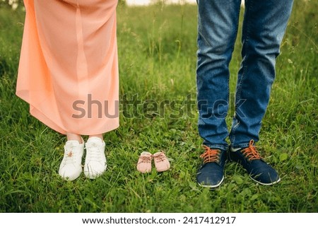 Future mom and dad feet with little baby shoes on the grass. Happy young family awaiting baby, love and happiness, new life concept