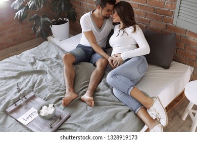 Future Mom And Dad Lying On The Bed Together, Thinking About Their Baby, Picking Up The Name. Man Touching Woman's Belly, Woman Put Her Head On Man's Shoulder. Safety And Love. Best Parents Ever