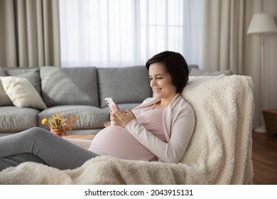 Future mom using phone. Happy young lady going to have a baby rest in chair at home hold smartphone read information about last months of pregnancy online. Millennial expectant mom using messenger app - Powered by Shutterstock