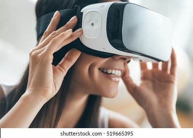 Future is now. Attractive young woman adjusting her VR headset and smiling while sitting at home 