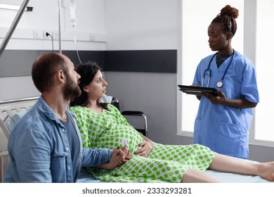 Future parents discussing with african american nurse before childbirh in hospital ward. Medical assistant typing patient contractions level on tablet computer, explaining pregnancy labor process - Powered by Shutterstock