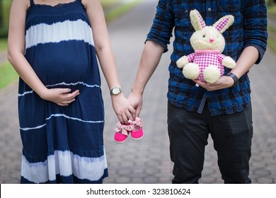 Future parents holding hands and a pair of little pink shoes - Powered by Shutterstock