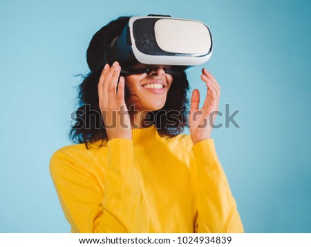 Future is right now. Confident young african american woman adjusting her virtual reality headset and smiling on blue background. Girl in VR goggles