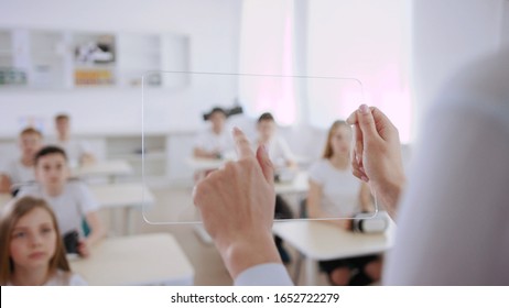 Future at school. Close-up of a female teacher holding a transparent special tablet in front of a class. Technology students using a transparent virtual tablet in the classroom in modern school. - Powered by Shutterstock