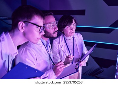 Futuristic Analysis: Three Scientists Delve into Device Study in Neon-Lit Science Center.