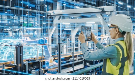 Futuristic Car Factory Digitalization Industry 4.0: Female Automotive Engineer Using Augmented Reality Tablet Computer To Scan Automated Robot Arm Assembly Line Manufacturing Electric Vehicles