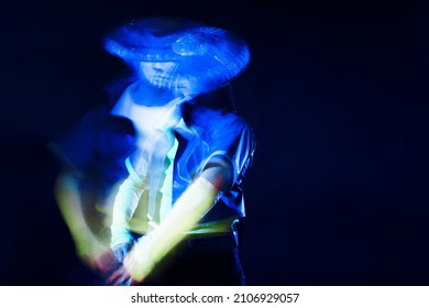 Futuristic Character In A Bright Stylized Outfit, Photo With Neon Colors. A Fantastic Character, A Cyber Mercenary, Long Exposure Photo With Blur Effect