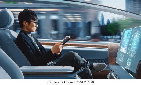 Futuristic Concept: Handsome Stylish Japanese Businessman in Glasses Reading Notebook and Watching News on Augmented Reality Screen while Sitting in a Autonomous Self-Driving Zero-Emissions Car. - Powered by Shutterstock