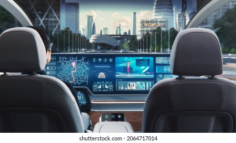 Futuristic Concept: Stylish Businessman Using Navigation App on an Augmented Reality Dashboard with Financial News Broadcast while Sitting in an Autonomous Self-Driving Zero-Emissions Electric Car. - Shutterstock ID 2064717014