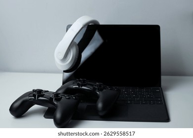 A futuristic gaming setup showcasing a tablet with keyboard, white over-ear headphones, two black game controllers. Perfect for illustrating cutting-edge gaming technolo - Powered by Shutterstock - Get 15% off with code: PIKWIZARD15