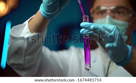 In a futuristic laboratory, a scientist with a pipette analyzes a colored liquid to extract the DNA and molecules in the test tubes