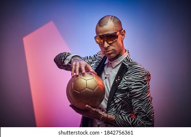 Futuristic man in suit with short haircut and eyewears poses with golden ball in colored abstract background. - Powered by Shutterstock