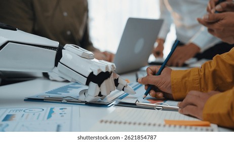 A futuristic robotic hand assists business professionals in a dynamic office meeting, showcasing collaboration, data analysis, and innovative technology in action.Noogenesis