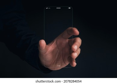 Futuristic transparent glass phone Technology. Super slim transparent future smartphone with vertical mock-up blank screen in hand on dark background.