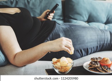 g, sedentary lifestyle, compulsive overeating. Obese woman laying on sofa with smartphone eating chips - Shutterstock ID 1124205980