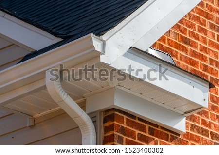 Gable with brick and vinyl siding, white frame gutter guard system, fascia, drip edge, soffit, on a pitched roof attic at a luxury American single family home neighborhood USA