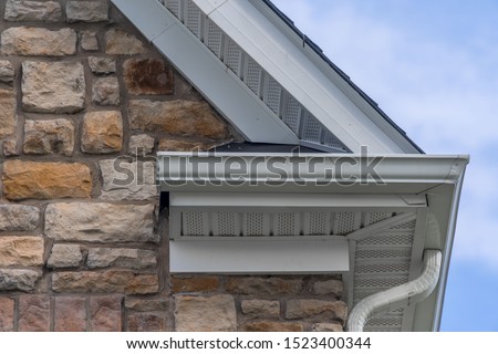 Gable with colored stone siding, white frame gutter guard system, fascia, drip edge, soffit, on a pitched roof attic at a luxury American single family home neighborhood USA

