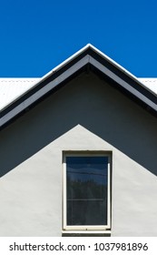 Gable of house with window and deep shadow under clear blue sky