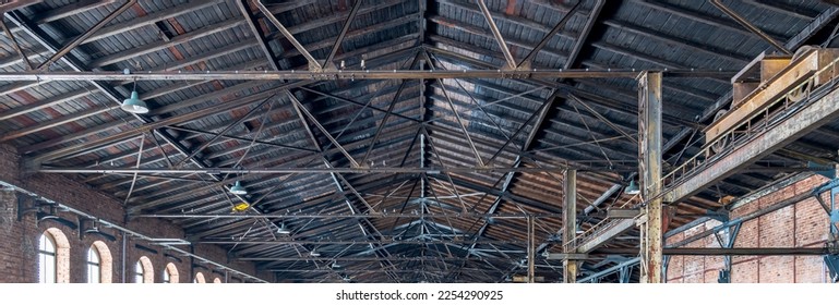Gable roof truss of a large, vintage factory hall. Roofing construction 
(sheathing) made of wooden planks. Brick walls and arcade windows. Industrial interior. - Shutterstock ID 2254290925