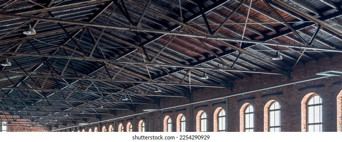 Gable roof truss of a large, vintage factory hall. Roofing construction 
(sheathing) made of wooden planks. Brick walls and arcade windows. Industrial interior. - Shutterstock ID 2254290929